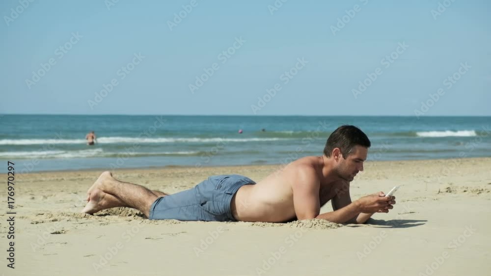 Young man lies on the beach by the sea with a mobile phone Young man lies on the beach by the sea with a mobile phone