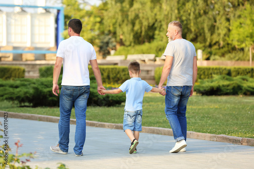 Little boy with daddy and grandfather walking in park
