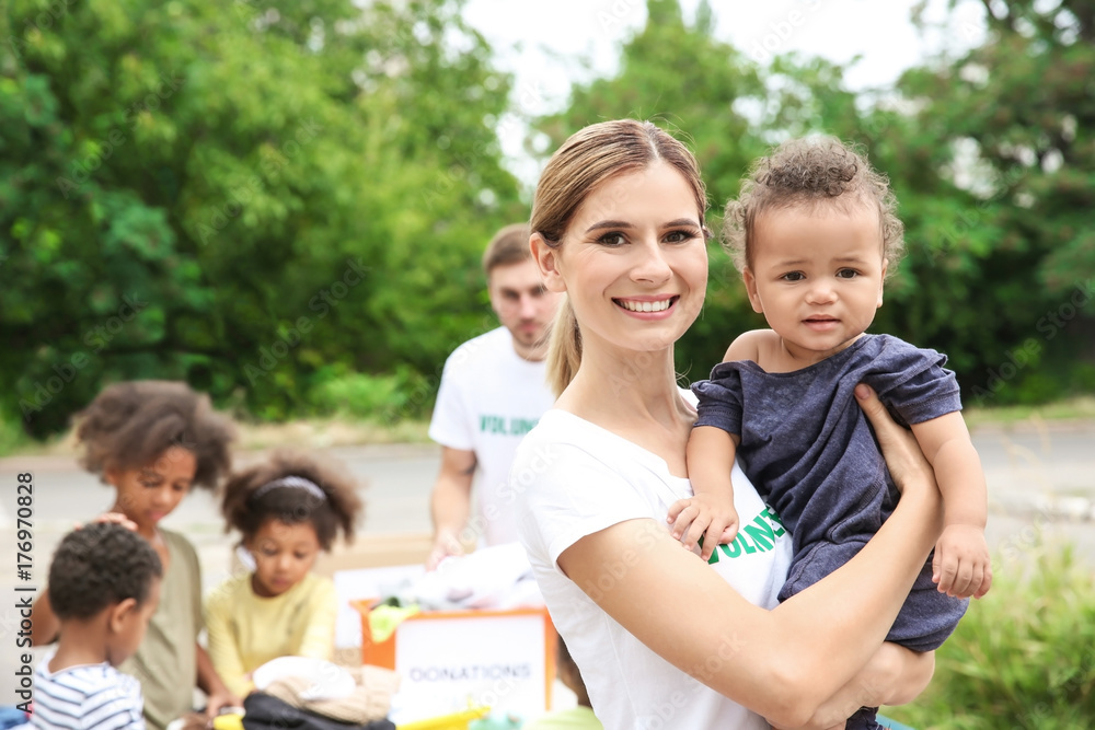 Young female volunteer holding little African girl outdoors Young female volunteer holding little African girl outdoors