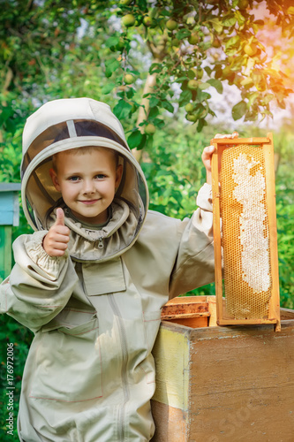 A boy beekeeper at the hive holds a honeycomb with honey in his hands. Apiary. Apiculture.