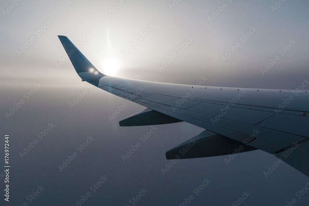 Obraz premium Skrzydło samolotu i słońce przeświecające przez mgłę chmur.