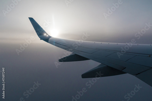 Wing of airplane and the sun shining through the fog of clouds.