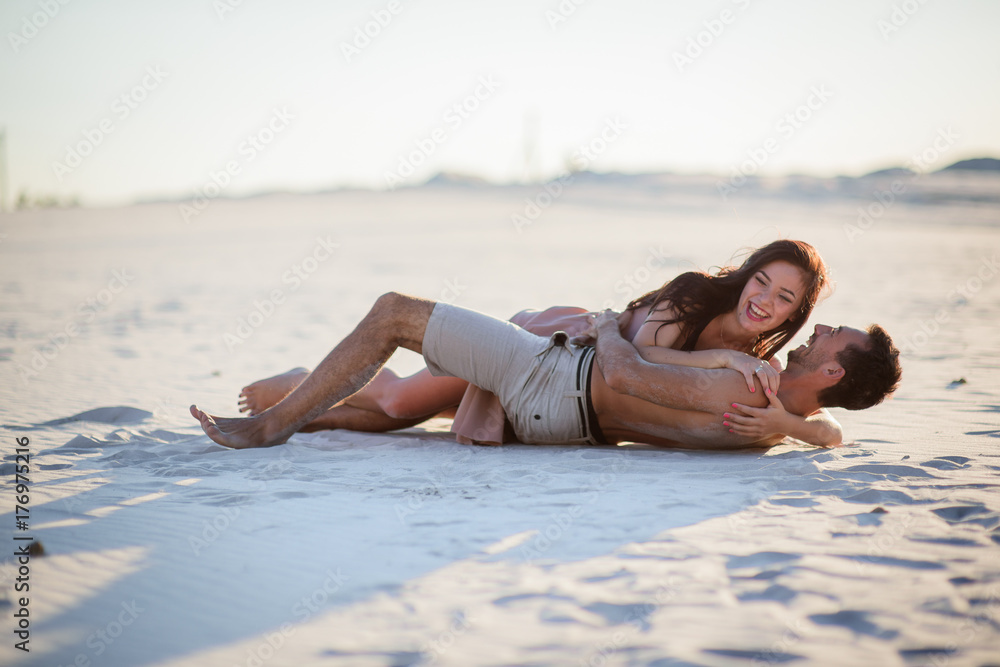 Woman hugs her nakes man lying on white sand
