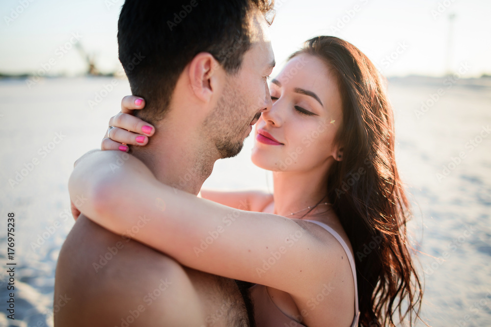 Fototapeta premium Gorgeous brunette hugs her man on white sand