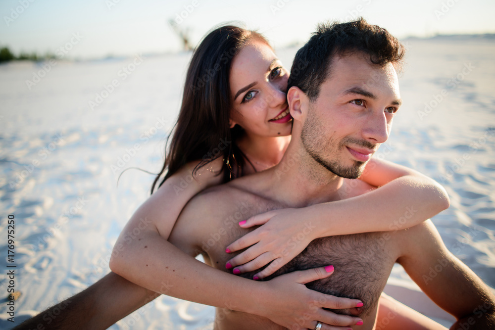 Woman hugs her man tender sitting on white sand Woman hugs her man tender sitting on white sand