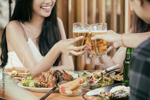 Beautiful Asian women are holding a glass of beer and cheers with her friends. She have smiling face and laughter.