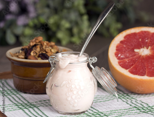 Jar with homemade yogurt. Granola from several types of cereals with nuts, coconut shavings and dried cranberries. And grapefruit