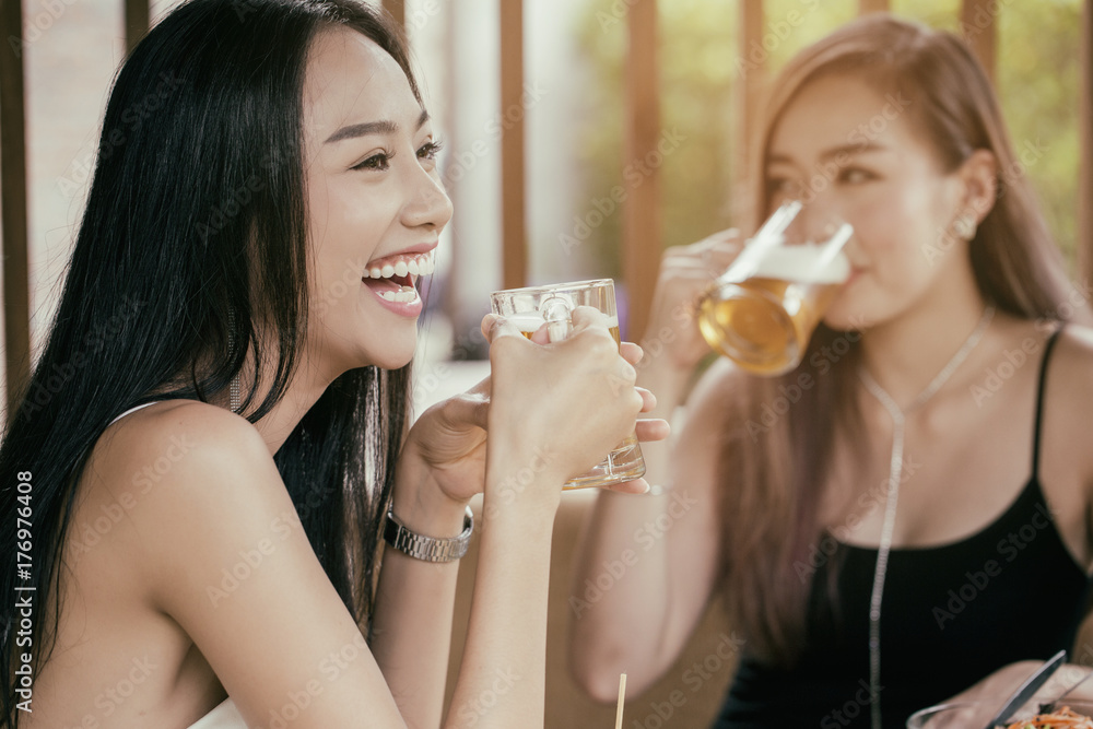 Beautiful Asian women are holding a glass of beer and cheers with her friends. She have smiling face and laughter. Beautiful Asian women are holding a glass of beer and cheers with her friends. She have smiling face and laughter.