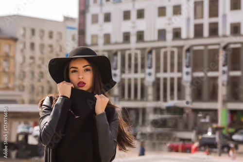 Fashion portrait of young gorgeous model wears wide-brimmed hat. Lady posing on a background of city