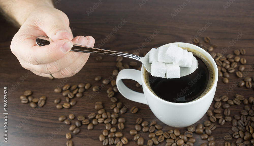 Hand holding a large spoonful of sugar cubes over a cup of coffee Hand holding a large spoonful of sugar cubes over a cup of coffee