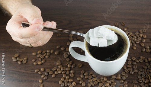 Hand holding a large spoonful of sugar cubes over a cup of coffee