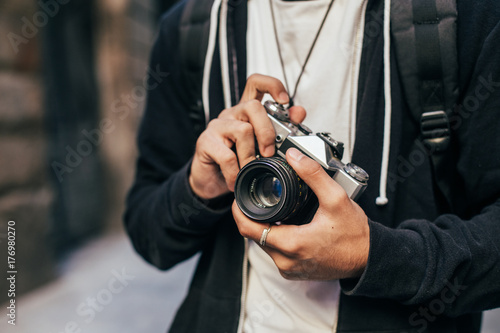 Closeup of man in hipster outfit, black hoodie cardigan and white tshirt, holding vintage analog film camera, zooming and focusing