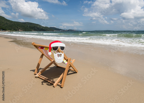 Fototapeta Naklejka Na Ścianę i Meble -  Deck chair at the tropical beach with Santa Claus sunglasses