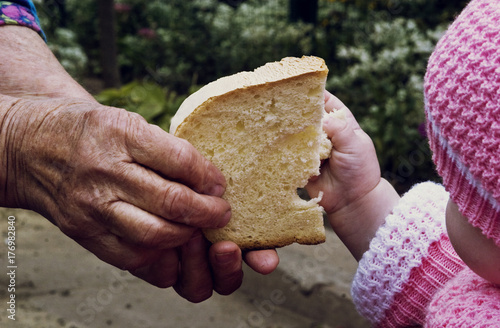 An old grandmother gives a piece of bread to a small child close up