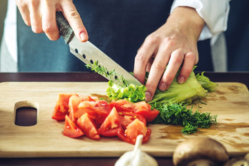 The chef in black apron cuts vegetables. Concept of eco-friendly products for cooking