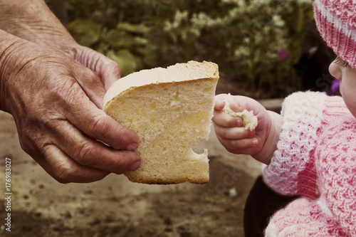A small child takes a slice of bread from the hands of an old grandmother
