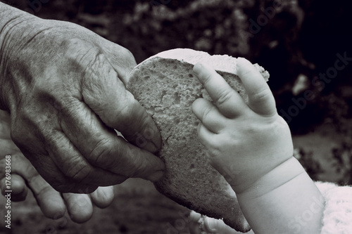 Old hand of a grandmother and a young child with a slice of bread close-up photo