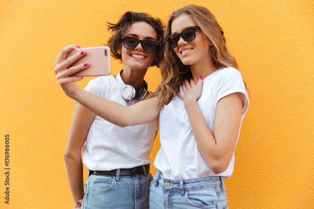 Two cheery young teenage girls in sunglasses taking a selfie Two cheery young teenage girls in sunglasses taking a selfie