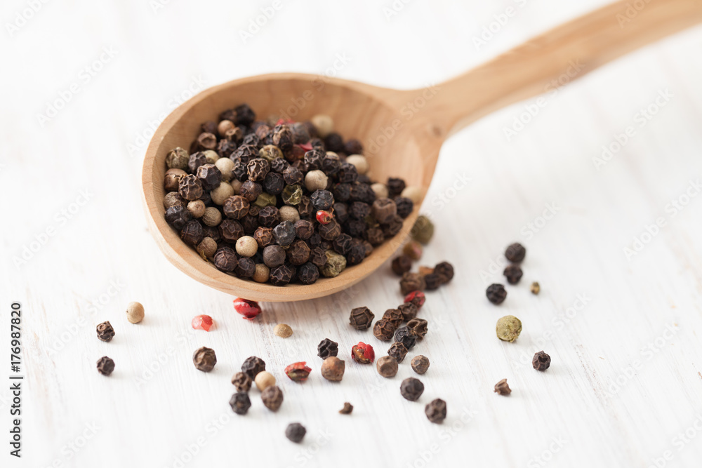 Red, white and black pepper in wooden spoon on white wooden table Red, white and black pepper in wooden spoon on white wooden table