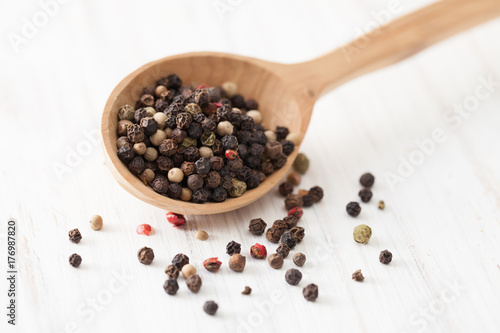 Red, white and black pepper in wooden spoon on white wooden table