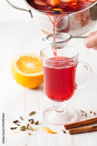 The pouring mulled wine into a glass through a strainer on the kitchen table