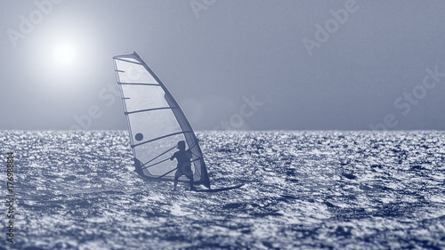 Windsurfer silhouette against a sunset background. Windsurfer Surfing The Wind On Waves, Recreational Water Sports, Extreme Sport Action. Sporting Activity. Healthy Active Lifestyle. Summer Fun