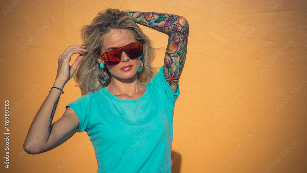 Beautiful blonde in sunglasses posing at the camera. Portrait on the  background of bright orange wall. Modern hipster girl with tattoos. Closeup  portrait. Stock Photo | Adobe Stock