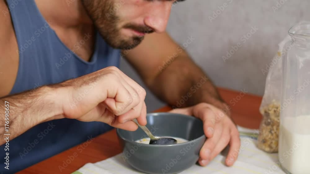 Attractive Young Man Eating Breakfast, Having some Cereal with Milk at Home in the Kitchen Attractive Young Man Eating Breakfast, Having some Cereal with Milk at Home in the Kitchen
