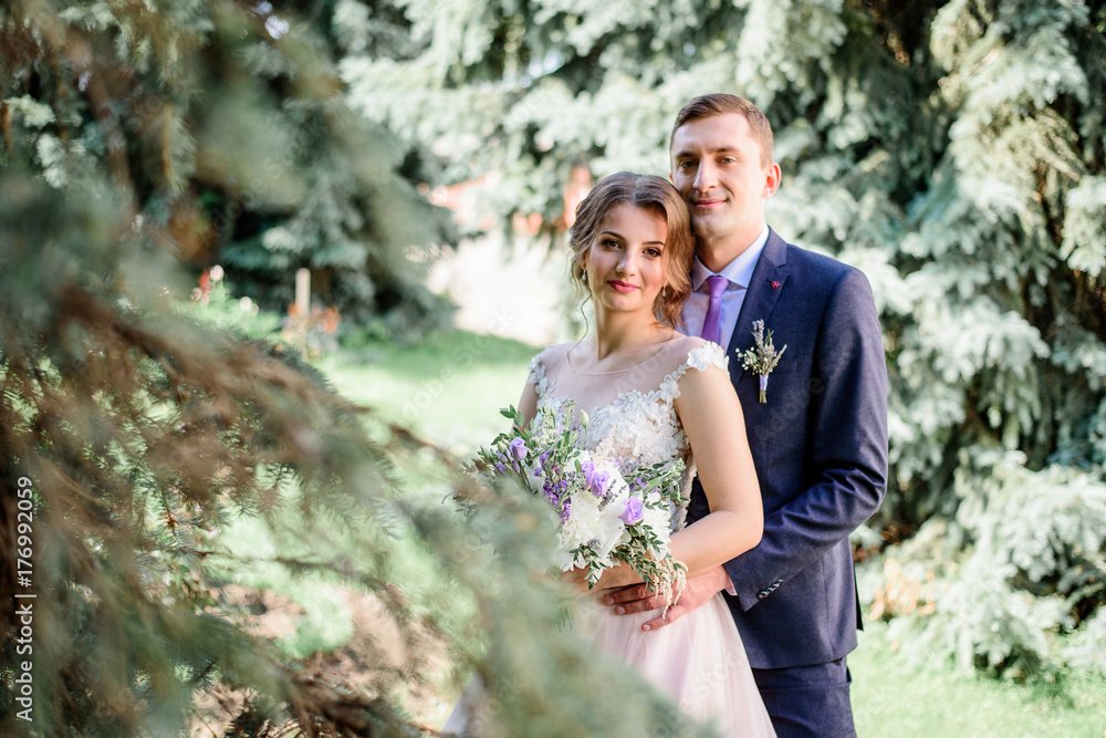 Groom hugs pretty bride tender standing in the green park Groom hugs pretty bride tender standing in the green park