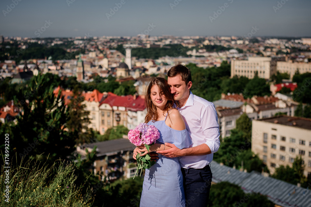 Fototapeta premium Man hugs woman tender standing before beautiful cityscape