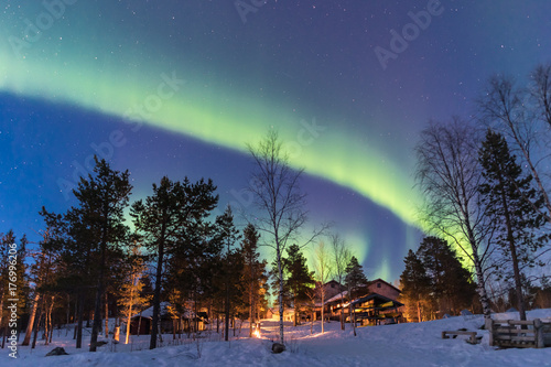 Green Northern lights belts in a blue sky over a cottage in the lapland forest photo