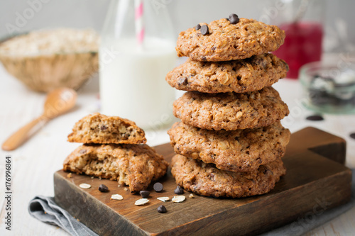Stack of oatmeal cookies with chocolate on a light background with flakes and a bottle of milk. Selective focus.