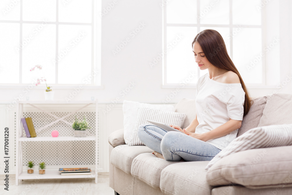 Young women using laptop sitting on sofa in white livingroom Young women using laptop sitting on sofa in white livingroom