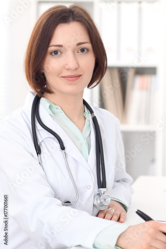 Young brunette female doctor sitting at the table and working at hospital office. 