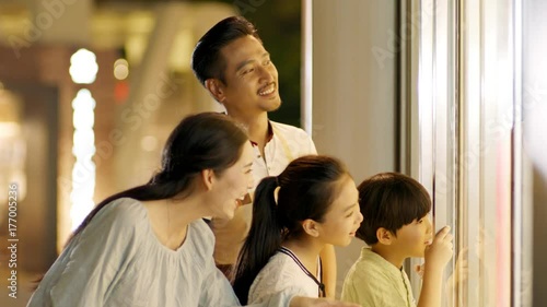 asian family of 4 standing & looking into shop window in slow motion