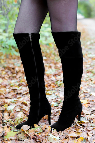 Women's legs in boots on leaves. Beautiful long female legs in black boots against a background of yellow autumn leaves. women's shoes on the autumn street