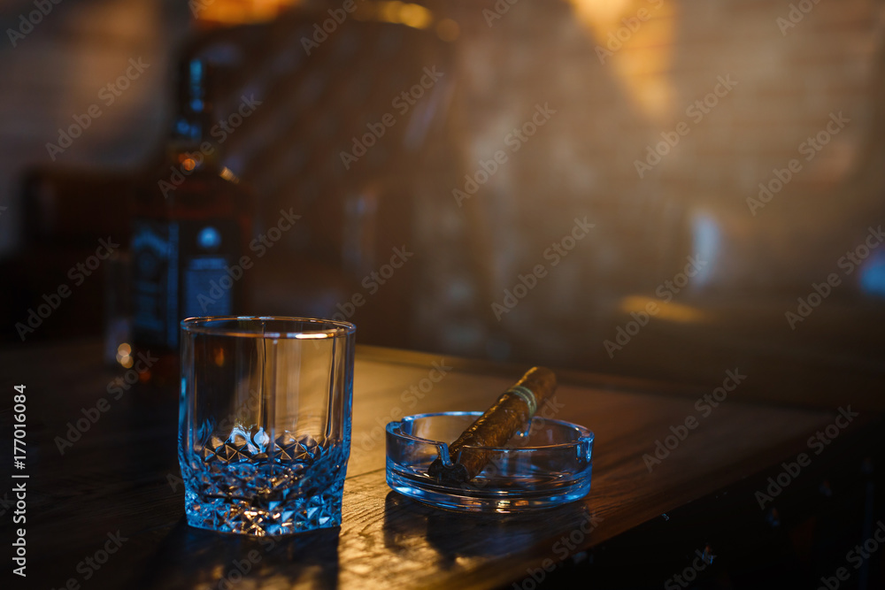 Glasses of whiskey with smoking cigar and ice cubes on wooden table Glasses of whiskey with smoking cigar and ice cubes on wooden table