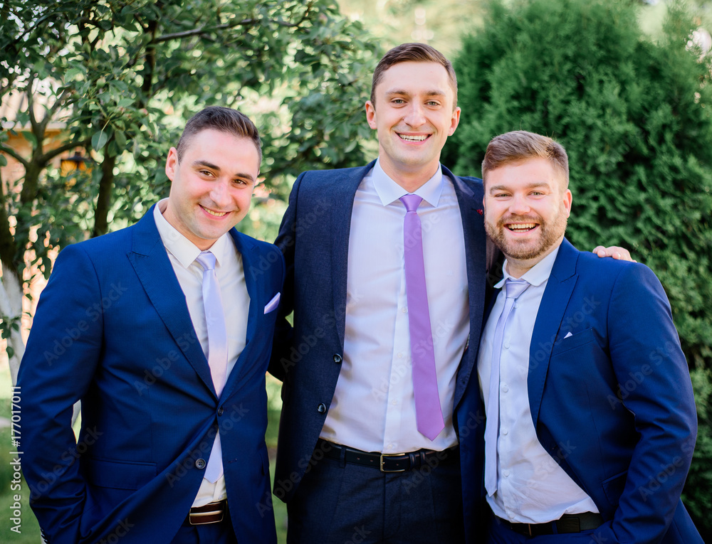 Three smiling men in blue suits pose in the garden Three smiling men in blue suits pose in the garden