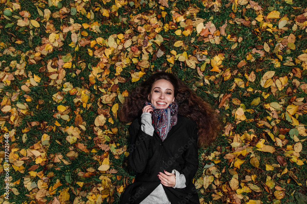 Fall portrait of a girl lying on a lawn in a forest park. Long hair on yellow foliage. Fall portrait of a girl lying on a lawn in a forest park. Long hair on yellow foliage.