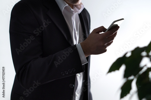 Mobile security, phisning and online crime. Businessman or man in a suit holding a smartphone in dark shadow. Financial fraud with smart device. photo