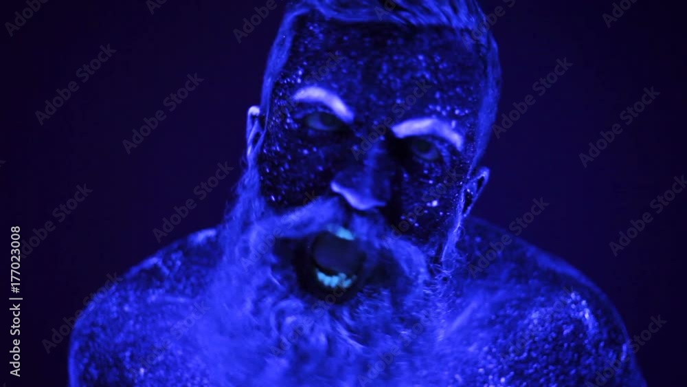 An evil man with a beard in the ultraviolet light is frighteningly screaming An evil man with a beard in the ultraviolet light is frighteningly screaming