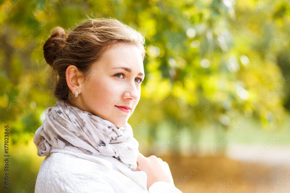 Young elegant woman in white coat standing in autumn park. Portrait of stylish girl in fall looking aside with copy space Young elegant woman in white coat standing in autumn park. Portrait of stylish girl in fall looking aside with copy space