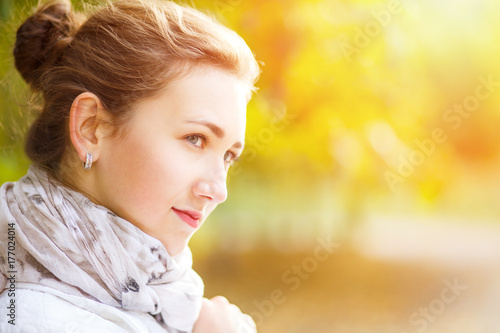 Young elegant woman in white coat standing in autumn park. Portrait of stylish girl in fall looking aside with copy space