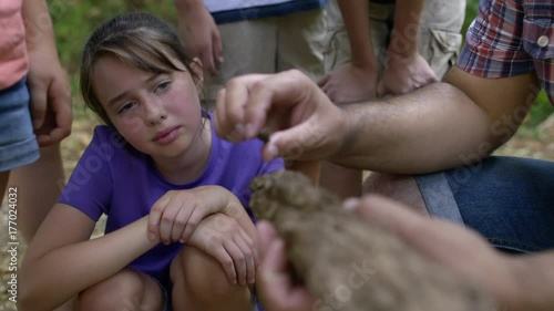 Focus on girl at summer camp learning about old branch from adult camp leader with group of children during outdoor class. Hand-held, slow motion 4K recorded at 60fps