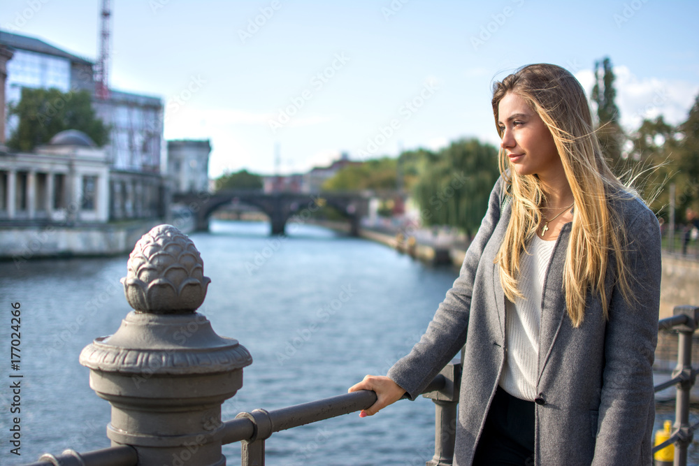 Young blonde woman standing near the river and enjoying a beautiful view.