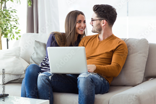 Beautiful young couple using laptop on the sofa at home.
