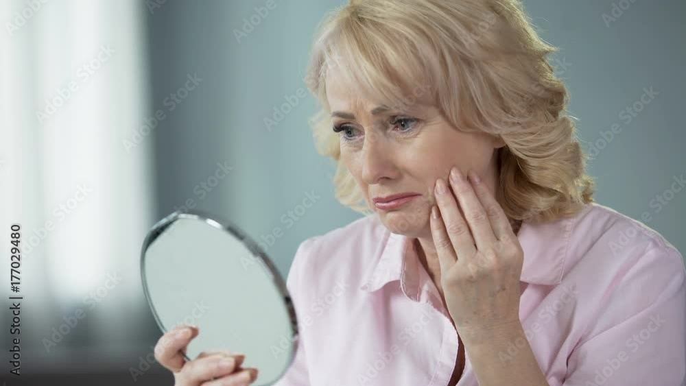 Sad woman looking at face reflection and crying, unhappy with wrinkled skin Sad woman looking at face reflection and crying, unhappy with wrinkled skin