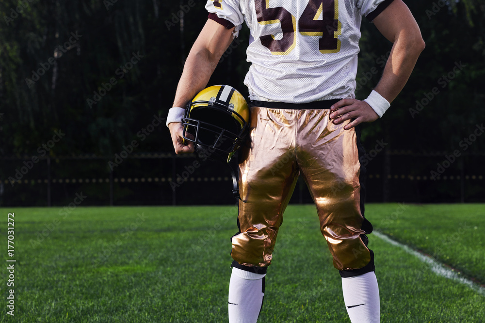 The American football player holding helmet on a background of green fields. The American football player holding helmet on a background of green fields.