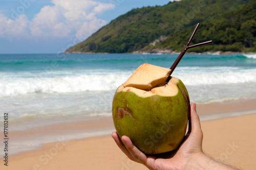 Coconut in hand on background of tropical beach.