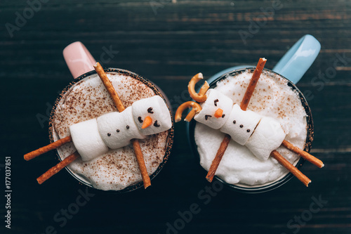 a mug with hot chocolate on a wooden table with a marshmallow man who is resting in a mug photo